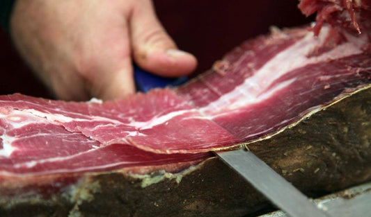 Croatian pršut being thinly sliced for a traditional Pršut i Sir appetizer
